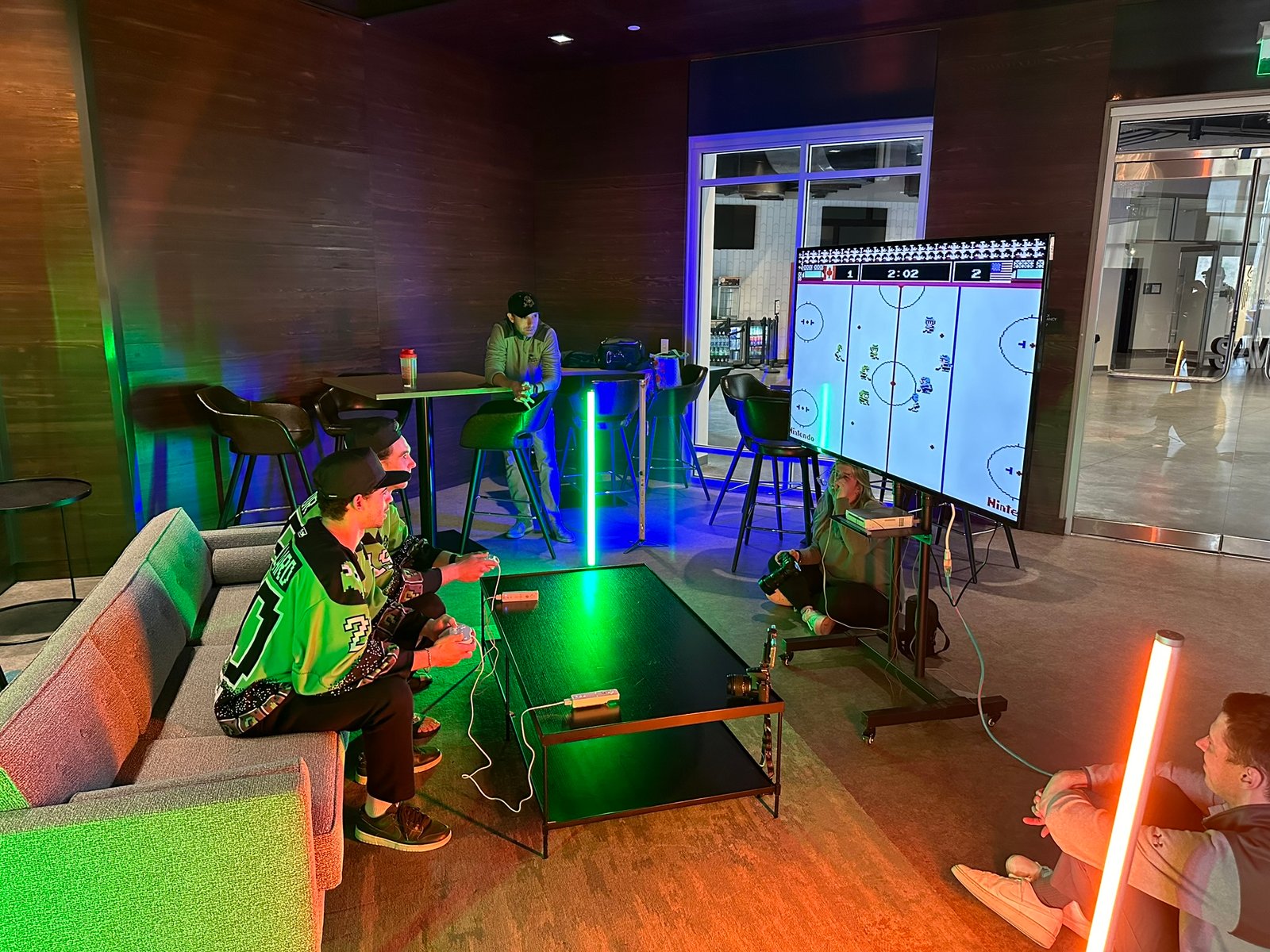 GPTV crew playing classic Nintendo hockey on a neon-lit lounge TV