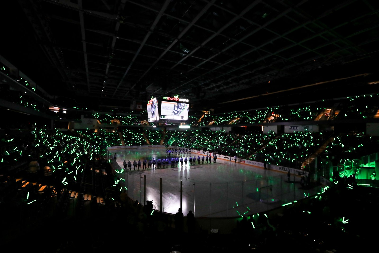 Teams lined up on the ice as fans wave green glow sticks during the All-Star Classic ceremony